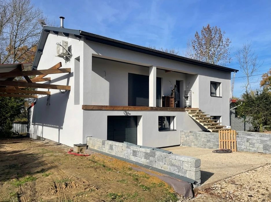 Maison individuelle neuve en cours de finition extérieure, façade enduit gris clair, toiture à deux pans ardoise noire