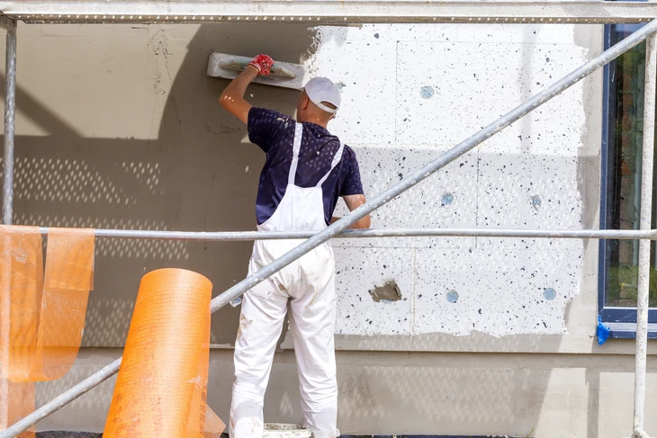 Chantier de rénovation extérieure avec ouvriers en vestes haute visibilité jaunes sur échafaudages métalliques